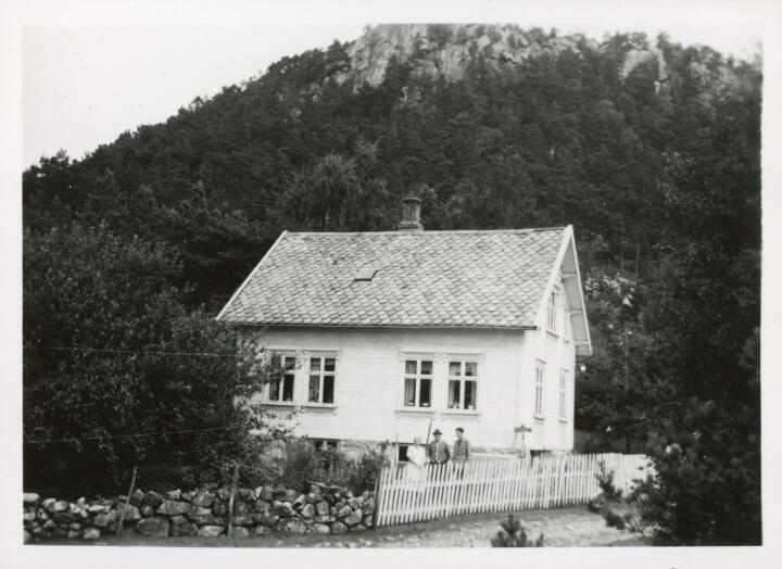 Marta Kristiansdtr. (Oaland) Bergsvik and her husband Berdinius Olaison Bergevik posing with an unknown person in front of their house in Bergsvik, Ryfylke. Date and photographer unknown.